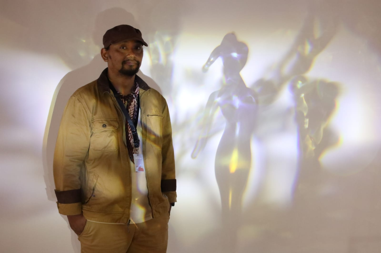 Bakau kaca karya Ivan Bestari memantulkan bayangan perempuan di dinding, mengajak kita merenung tentang kekuatan alam yang rapuh di tengah kerakusan manusia. (Foto:Robertus Riski)