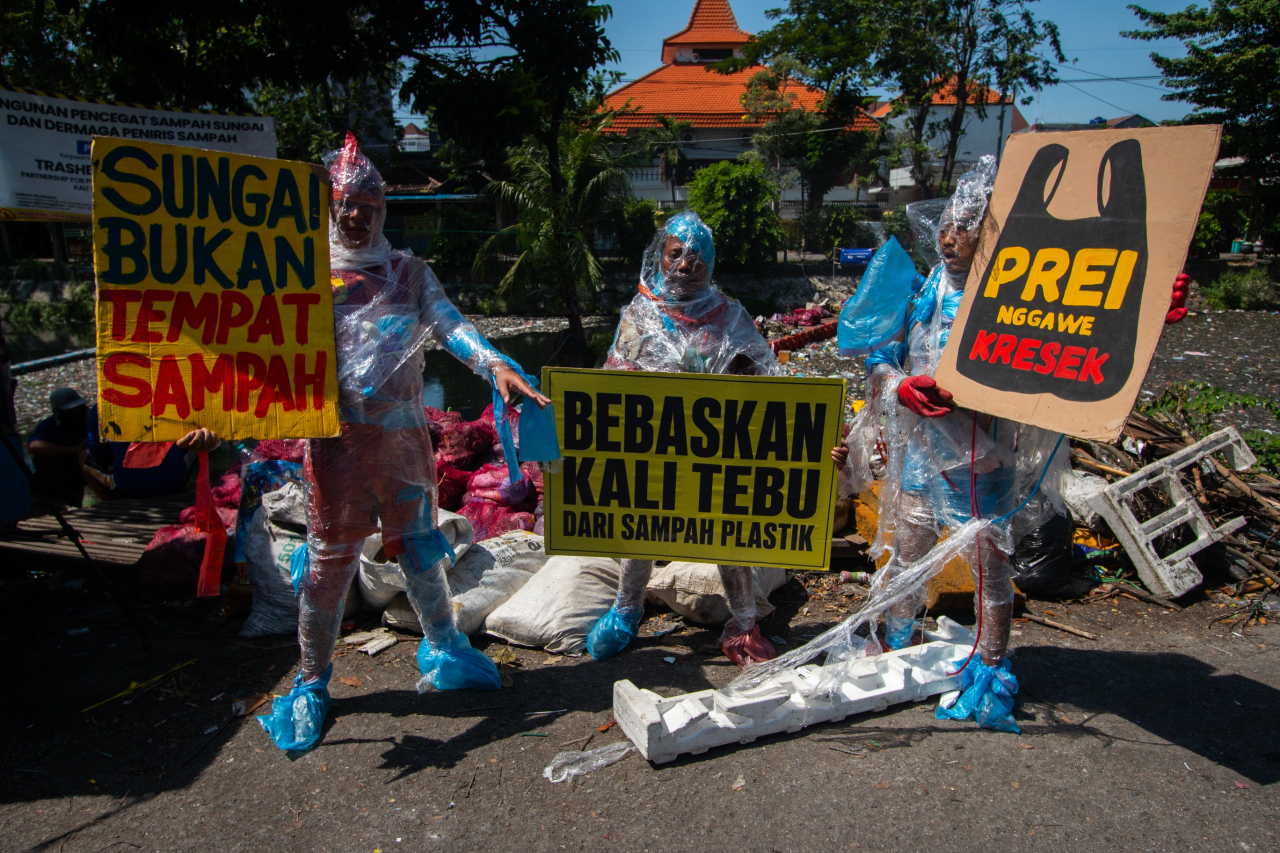 Tiga aktivis mengenakan kostum plastik dan topeng ikan saat aksi di tepi Kali Tebu, Surabaya, Rabu (24/6), sebagai simbol hilangnya biota sungai akibat pencemaran plastik. (Foto: M. Iffan)